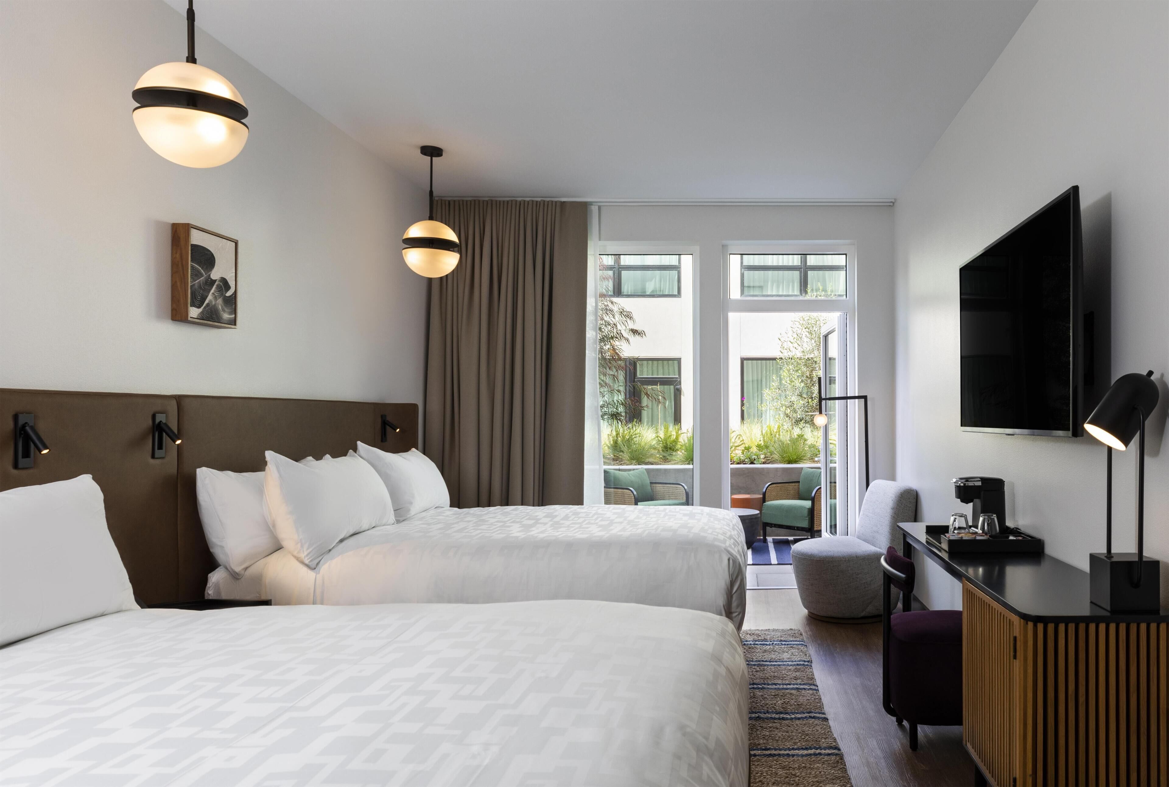 A hotel room with two beds, a TV, a desk, and a view of the outdoors.