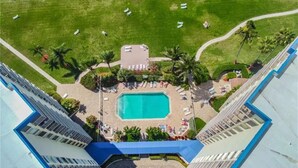 Luftaufnahme eines Hotels mit Schwimmbad, Liegestühlen und Palmen.