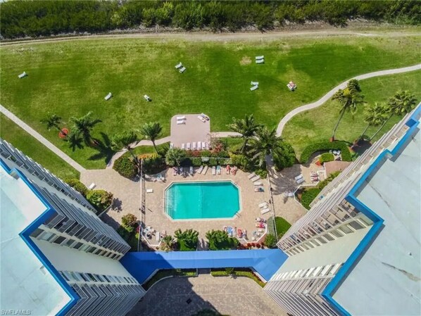 An aerial view of a hotel with a swimming pool, lounge chairs, and palm trees.