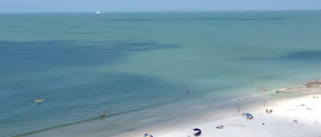 Ein Strand mit klarem türkisblauem Wasser, sandigem Ufer und mehreren Strandsonnenschirmen.