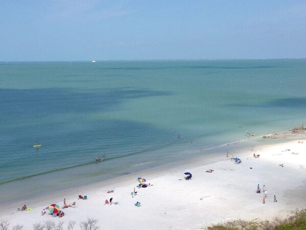 A beach with clear turquoise water, sandy shore, and several beach umbrellas.