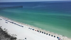 A beach with a long stretch of white sand, a pier extending into the water, and several umbrellas lined up along the shore. - 🌅 INCREDIBLE View ~ Free Beach Service..SPACIOUS-Remodeled Kitchen~Gulf Front 🏖️ (Navarre)