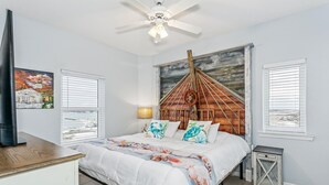 Un dormitorio con cama, ventilador de techo, un cuadro, lámpara y ventana con persianas.