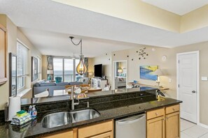 Una cocina moderna con un lavamanos doble, un comedor con vistas y una sala de estar con sofá y televisor.
