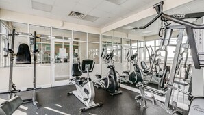 Ein Fitnessraum mit unterschiedlichen Trainingsgeräten, großen Fenstern und einer Spiegelwand.