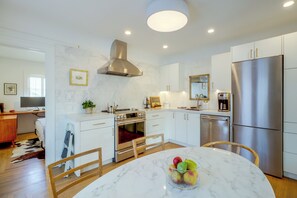 A modern kitchen with white cabinetry, stainless steel appliances, and a marble countertop. - Charming Midtown Brick Home: Walk to Truckee River (Reno)