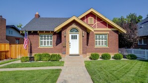 Une maison à deux étages avec une façade en briques, un porche à l’avant et un petit jardin devant.