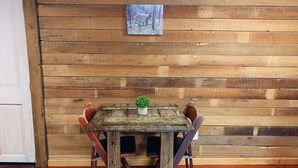 Een rustieke houten tafel met een kleine plant, omringd door vier stoelen, tegen een houten wand met een lijstwerk afbeelding.