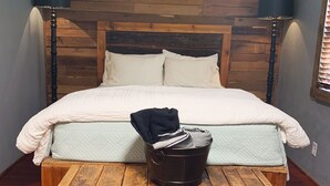 Een bed met een houten hoofdeinde, twee bedlampjes en een klein houten tafeltje met een emmer.