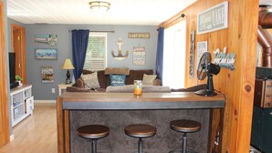 Zona de bar con taburetes, un ventilador y una barra de madera.