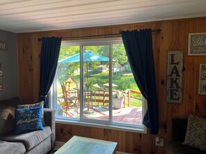 A cozy room with a large window, wooden walls, a couch, and a small table. - Up North Retreat - hot tub - pool table -arcade- sandy oasis- fire pits (Beaverton)