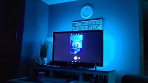 Una sala de estar con un televisor montado en la pared, un reloj y un cartel con una cita.