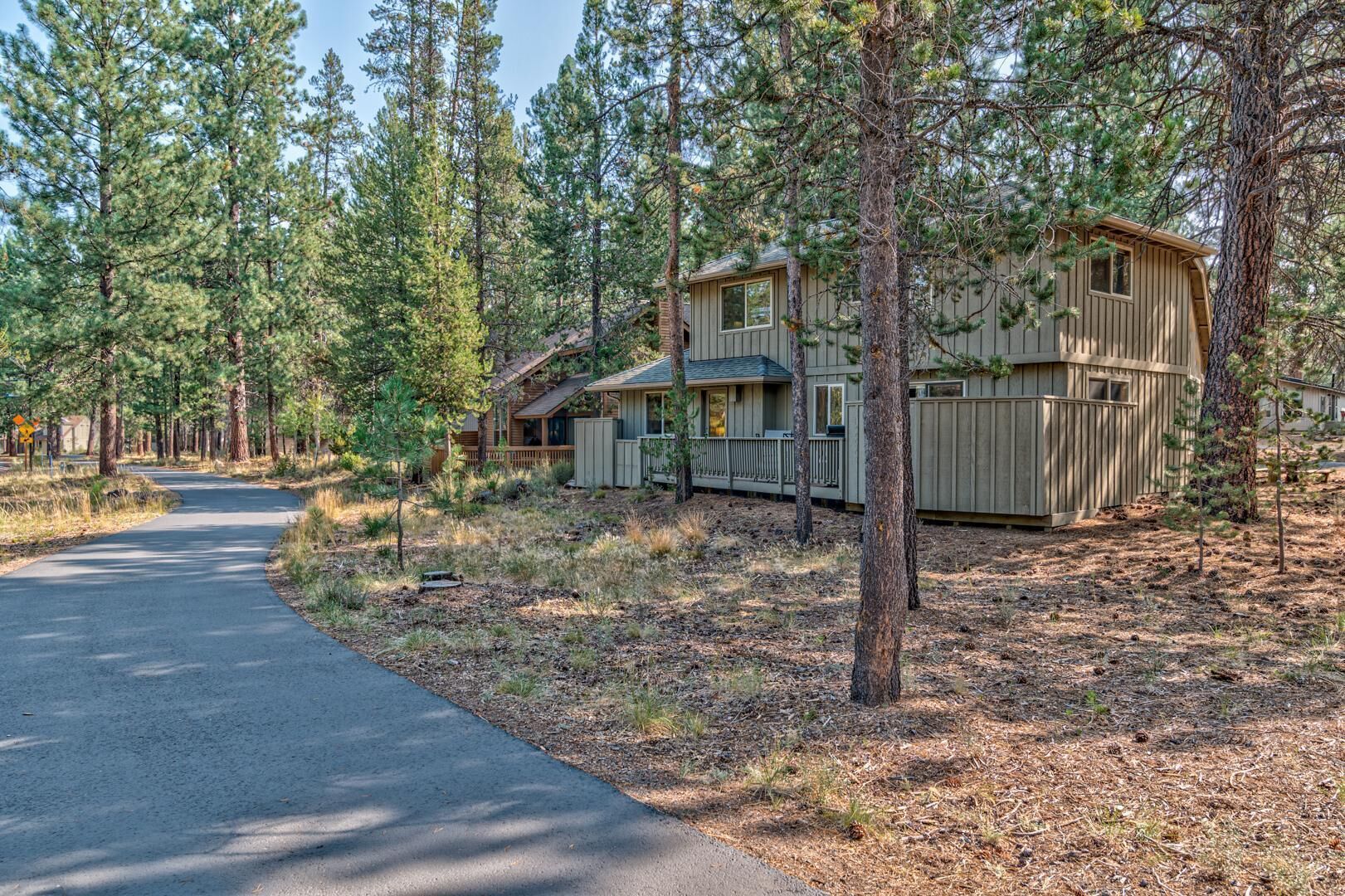 A cabin with a porch and a fenced yard, surrounded by tall pine trees.