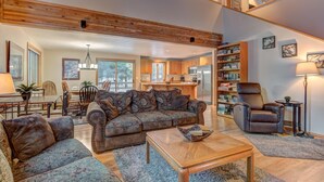 A spacious living room with a large sectional sofa, a coffee table, and a fireplace. There is a dining area with a table and chairs, and a kitchen in the background. - Ashwood Lane 1 (Bend)