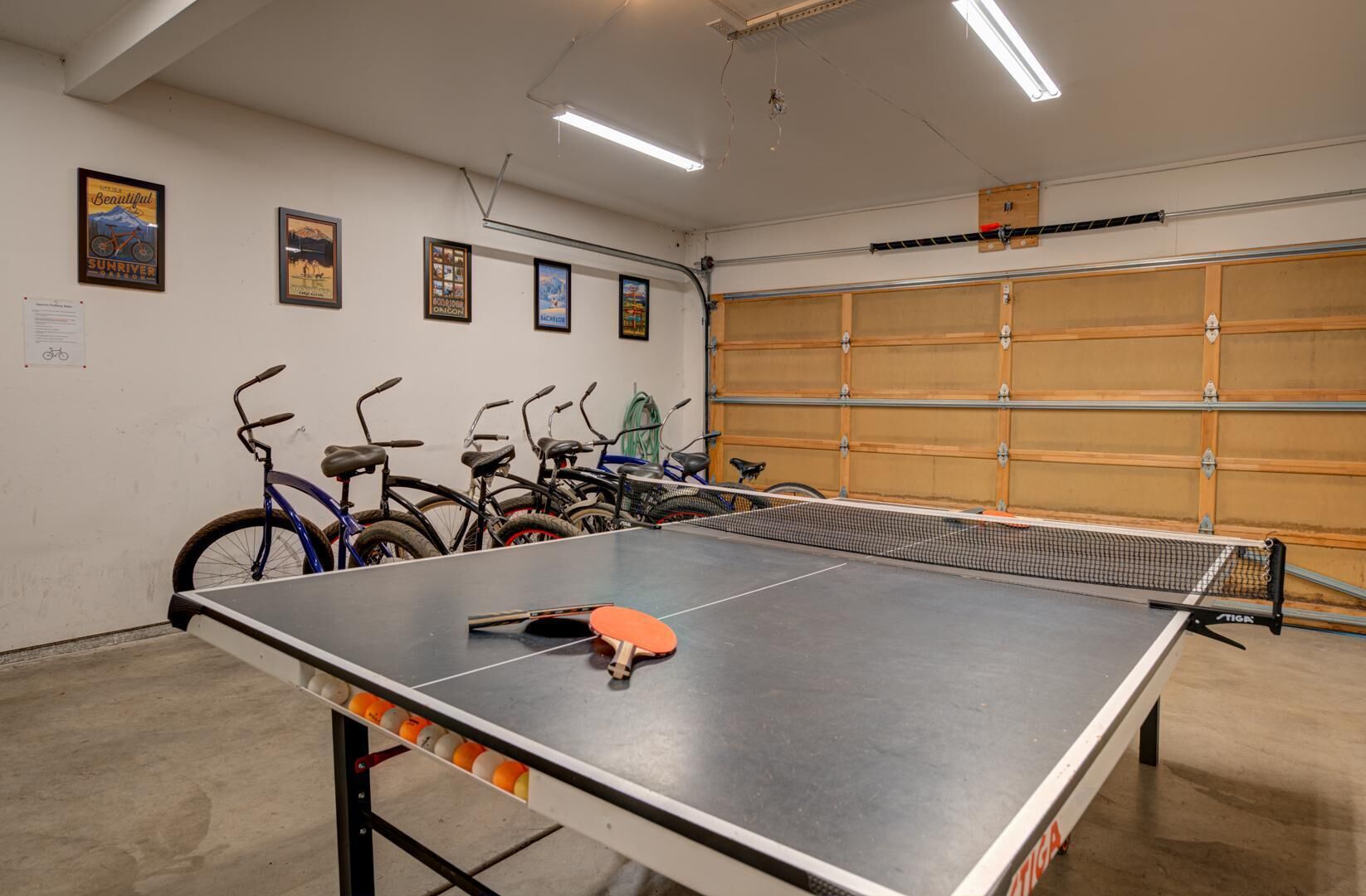 A ping pong table in a room with bicycles and a garage door.