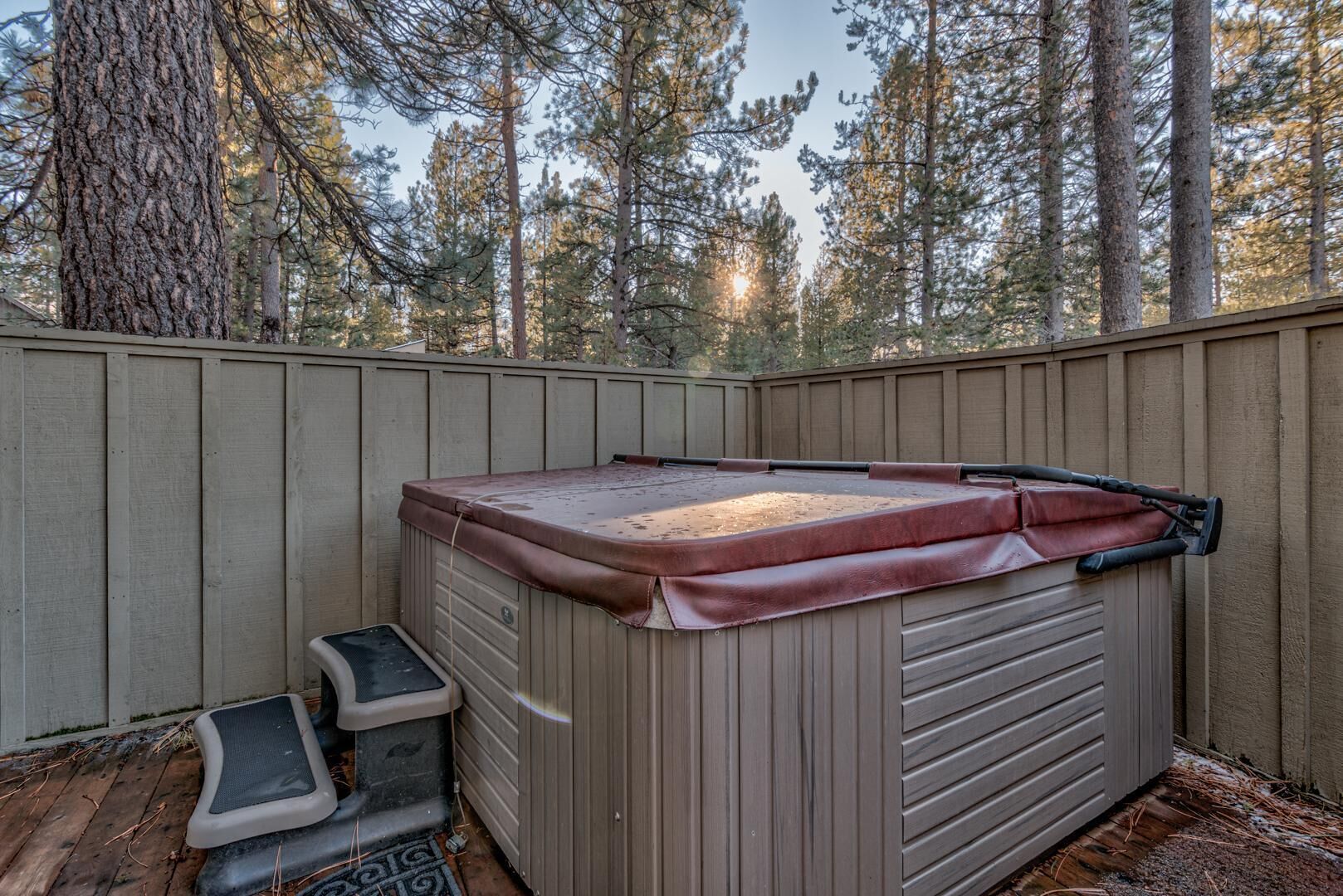 A hot tub in a backyard with a wooden deck and a wooden fence.