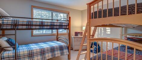 A bunk bed room with a window, a dresser, and a ladder.