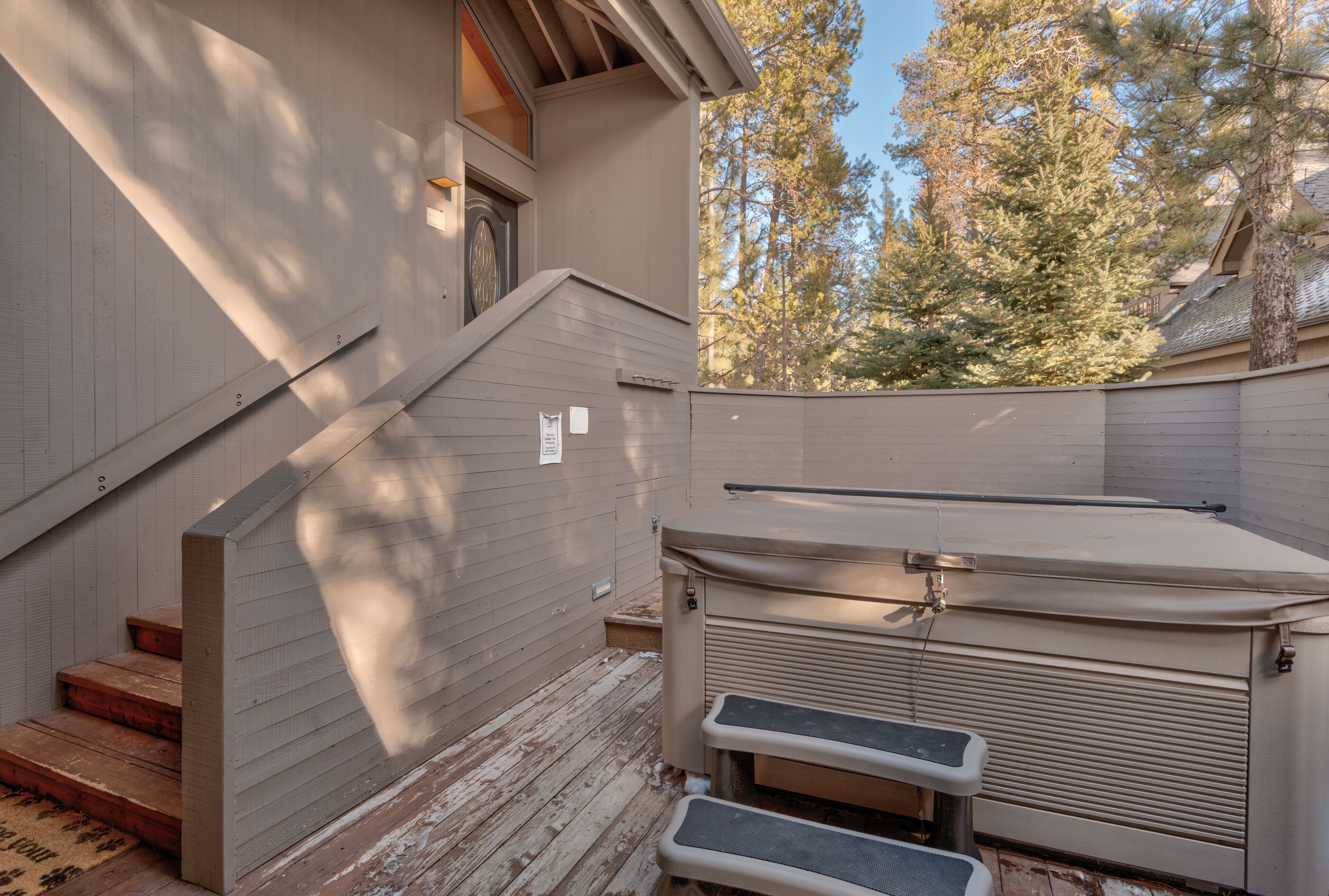 A covered outdoor area with a wooden deck, a built-in bench, and a small set of stairs leading to a door.