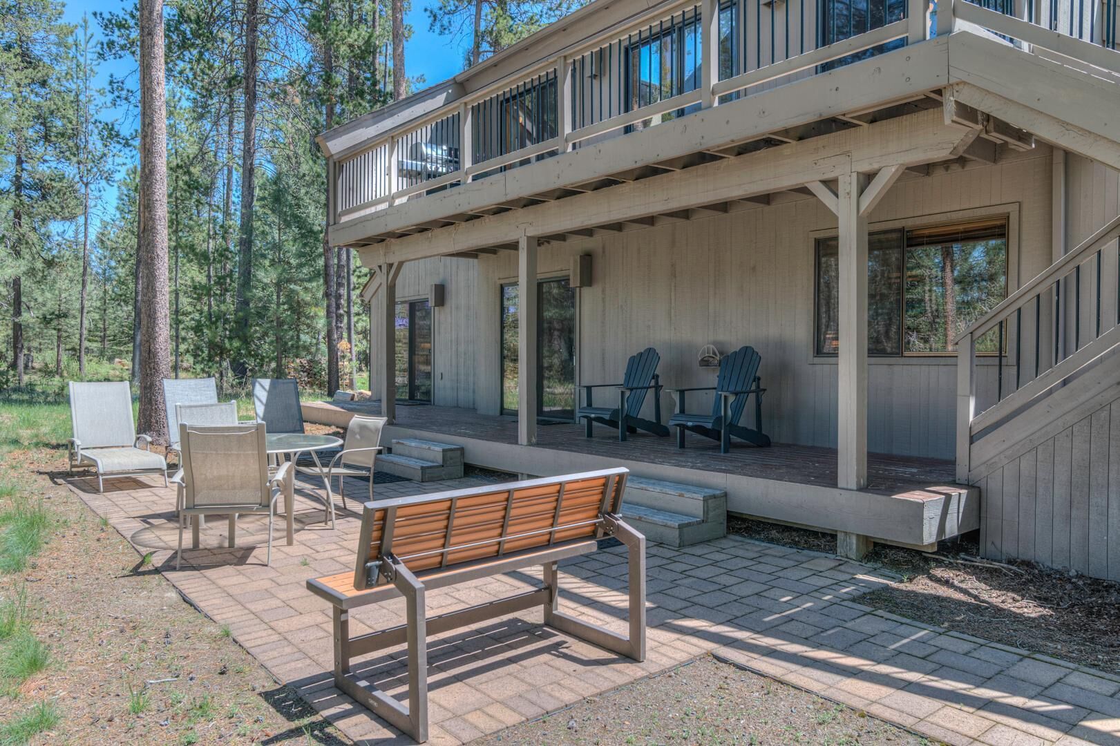 A modern cabin with a covered patio, outdoor seating, and a staircase leading to a deck.
