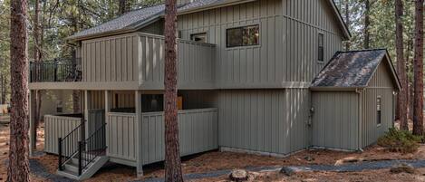 A two-story cabin with a balcony and a separate garage, surrounded by trees.