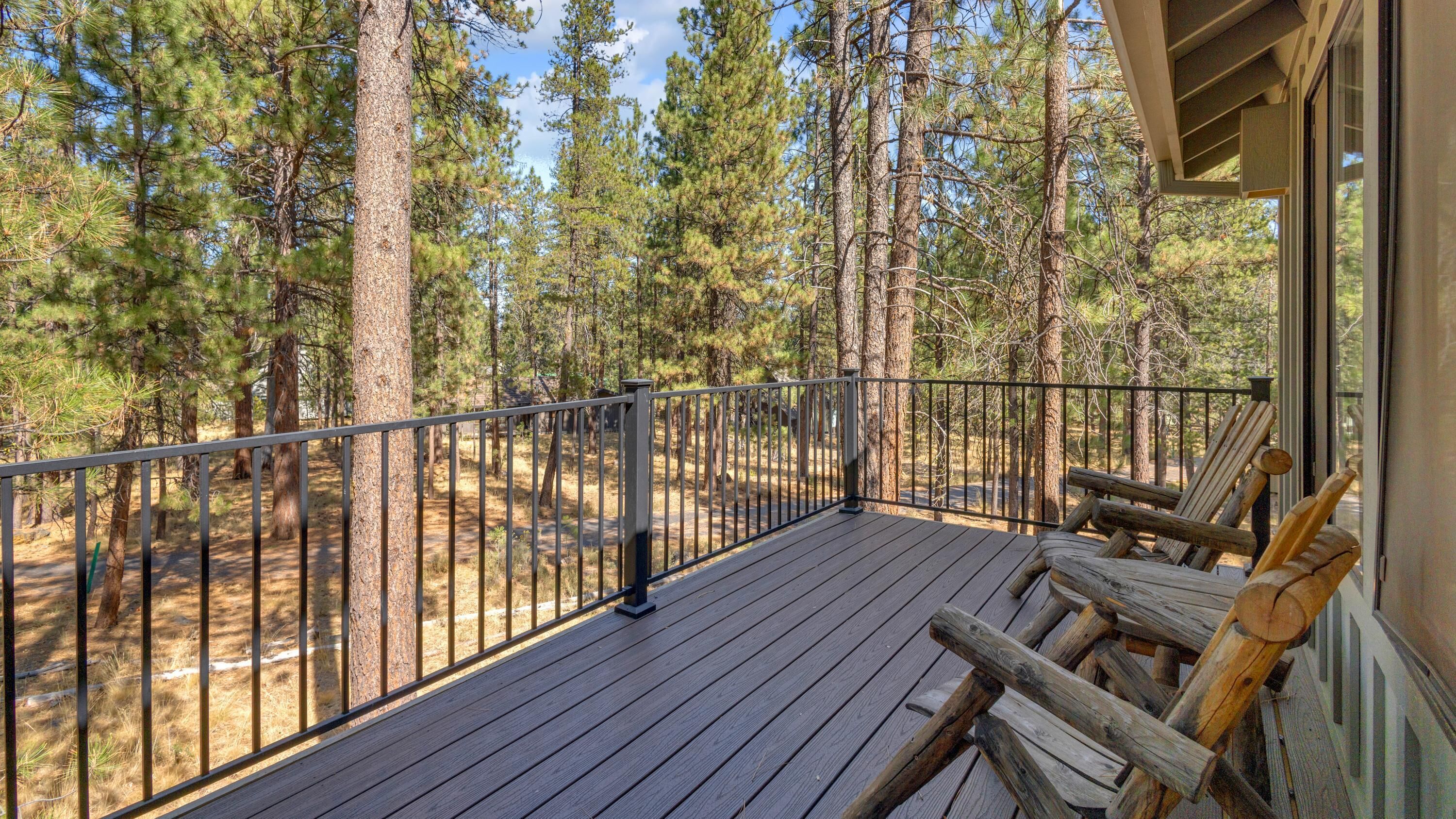 A wooden deck with metal railings overlooking a forested area.