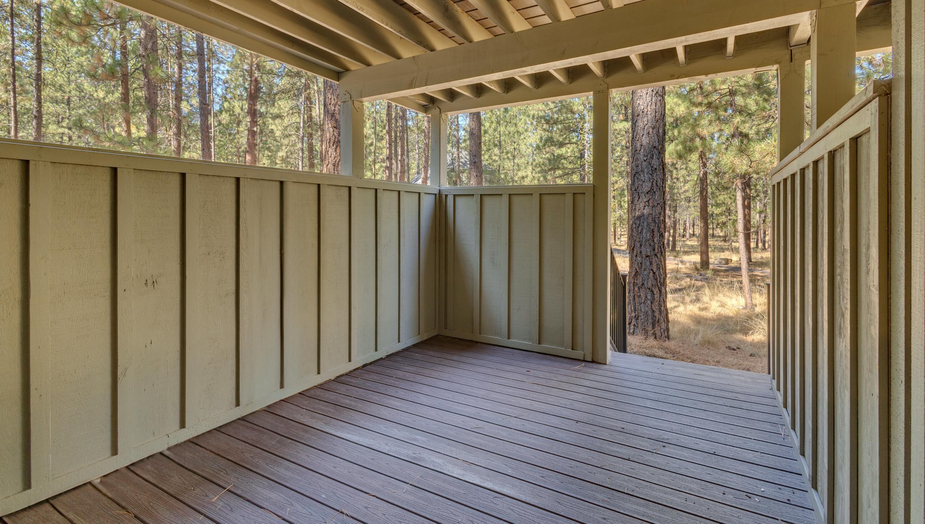 A covered wooden deck with a view of a forest.