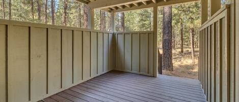 A covered wooden deck with a view of a forest.