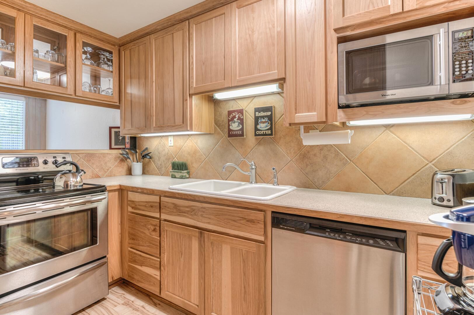 A kitchen with wooden cabinets, a stainless steel stove, a microwave, a dishwasher, and a toaster.