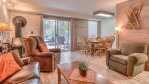 A spacious living room with a fireplace, leather sofas, a dining area, and a large window offering a view of the outdoors. - Abbot House Condo 8 (Bend)