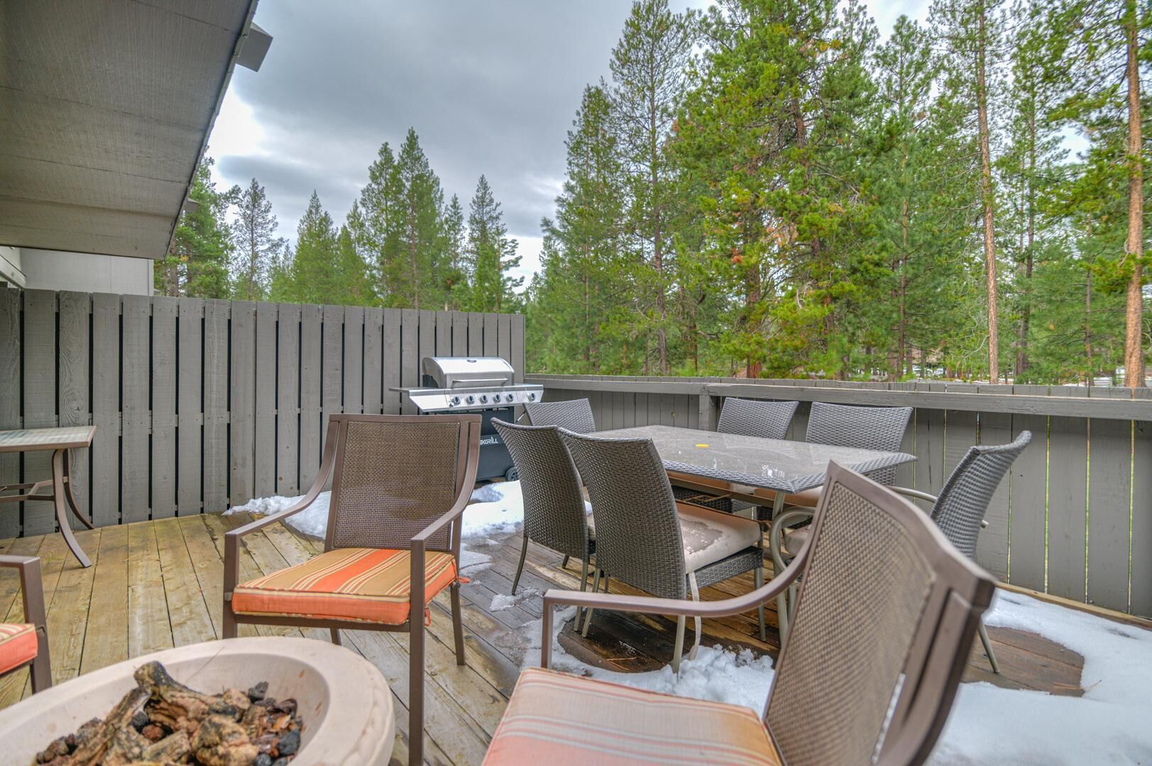 An outdoor patio with a grill, wicker furniture, and a view of trees.