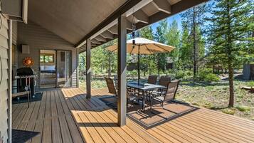 Una terraza techada al aire libre con mesa y sillas, una parrilla y vistas del bosque circundante.