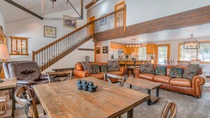 A spacious living room with a high ceiling, a wooden staircase, leather sofas, and a dining area with a wooden table. - Lassen Lane 3 (Bend)