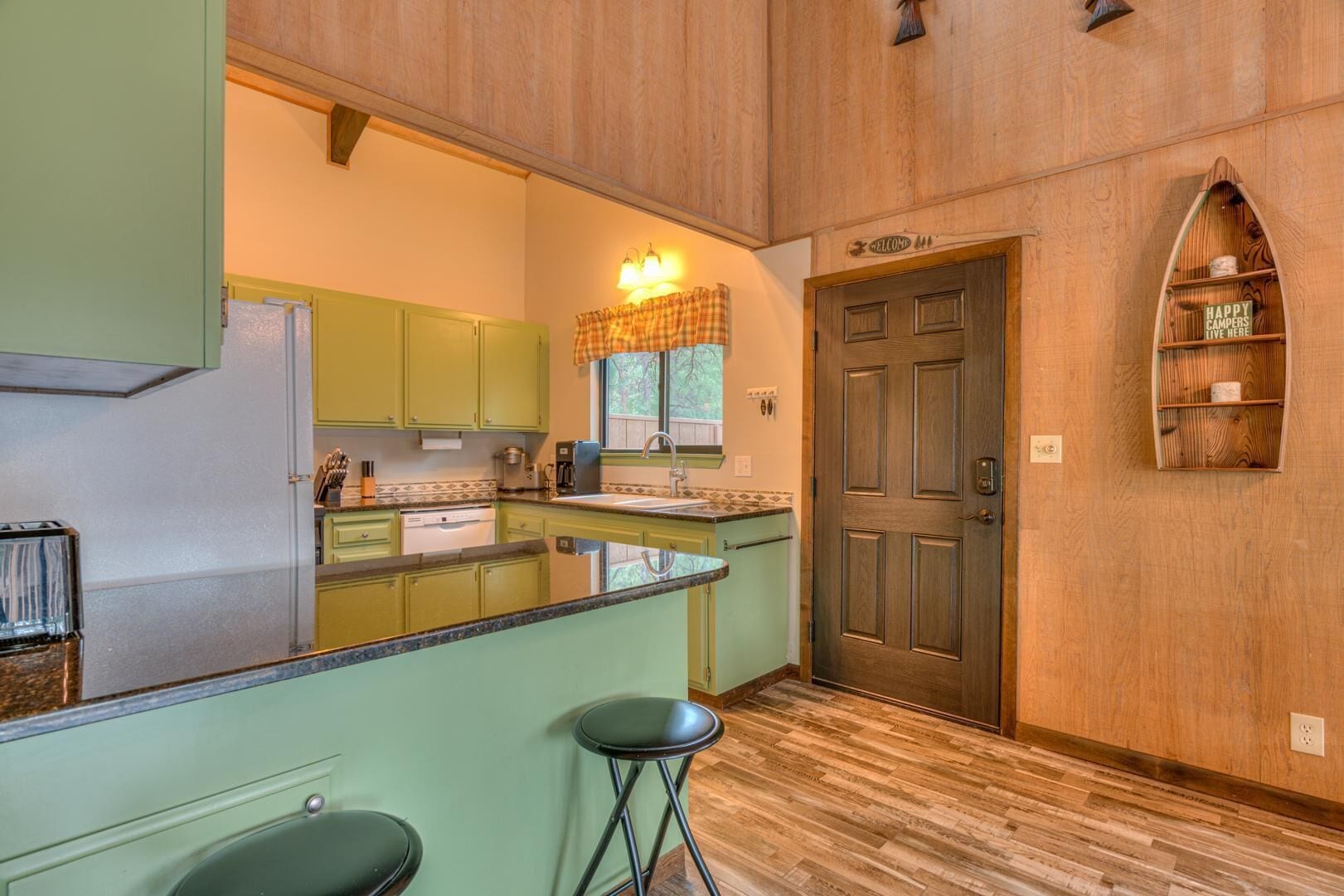 A kitchen with green cabinets, a wooden countertop, and a bar stool.