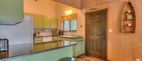 A kitchen with green cabinets, a wooden countertop, and a bar stool.