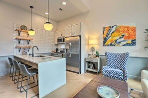 A modern kitchen with a central island, bar stools, a refrigerator, and pendant lighting. - Modern Downtown Birmingham Condo w/ Rooftop Access (Birmingham)