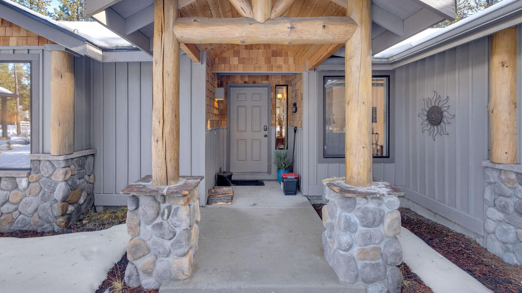 A covered porch with stone pillars, a stone wall, and a wooden ceiling.