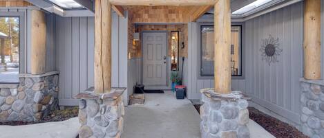 A covered porch with stone pillars, a stone wall, and a wooden ceiling.