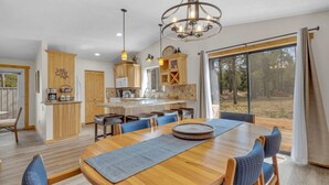 A modern kitchen with wooden cabinets, a central island, and a dining area with a wooden table and blue chairs. - Kinglet Lane 46 (Bend)