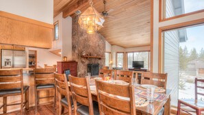 A spacious dining area with wooden furniture, a stone fireplace, and large windows offering a view of the outdoors.