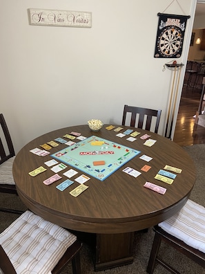 A Monopoly board game set on a round wooden table with chairs around it.