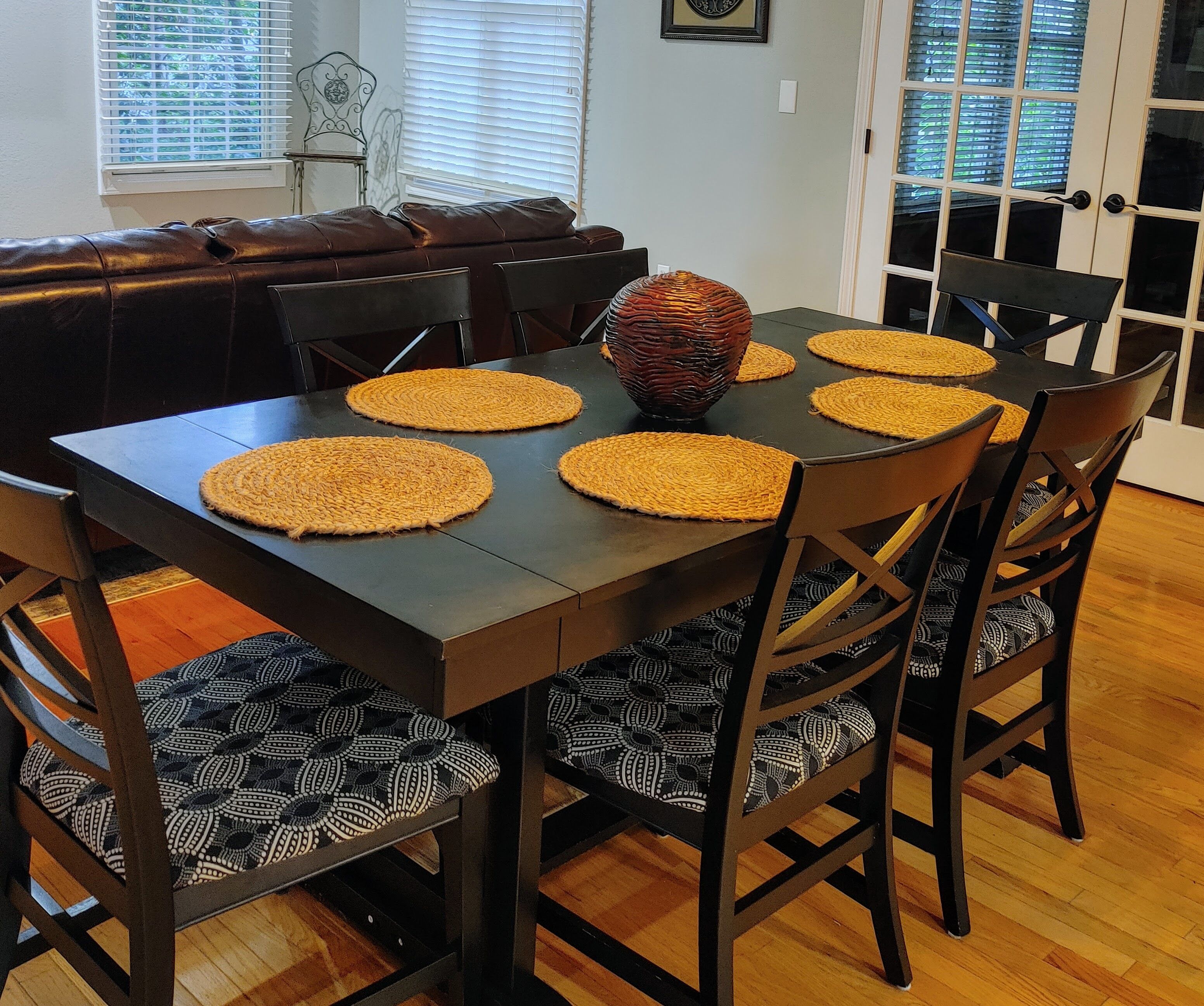 A dining table with four woven placemats, surrounded by wooden chairs with patterned cushions.