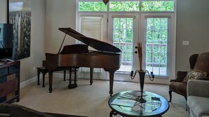A living room with a grand piano, a glass coffee table, and a television on a stand. - 5 bdr vacay everyone will LOVE (Loudon)