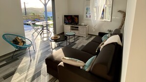 A modern living room with a sofa, a TV, and a dining area with chairs and a table.