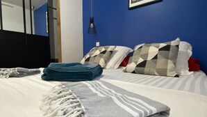 A neatly made bed with a striped blanket and a macrame throw, a blue wall with a framed picture, and a black headboard.