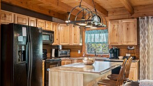 A kitchen with wooden cabinets, a black refrigerator, a microwave, a stove, and a large island with chairs.