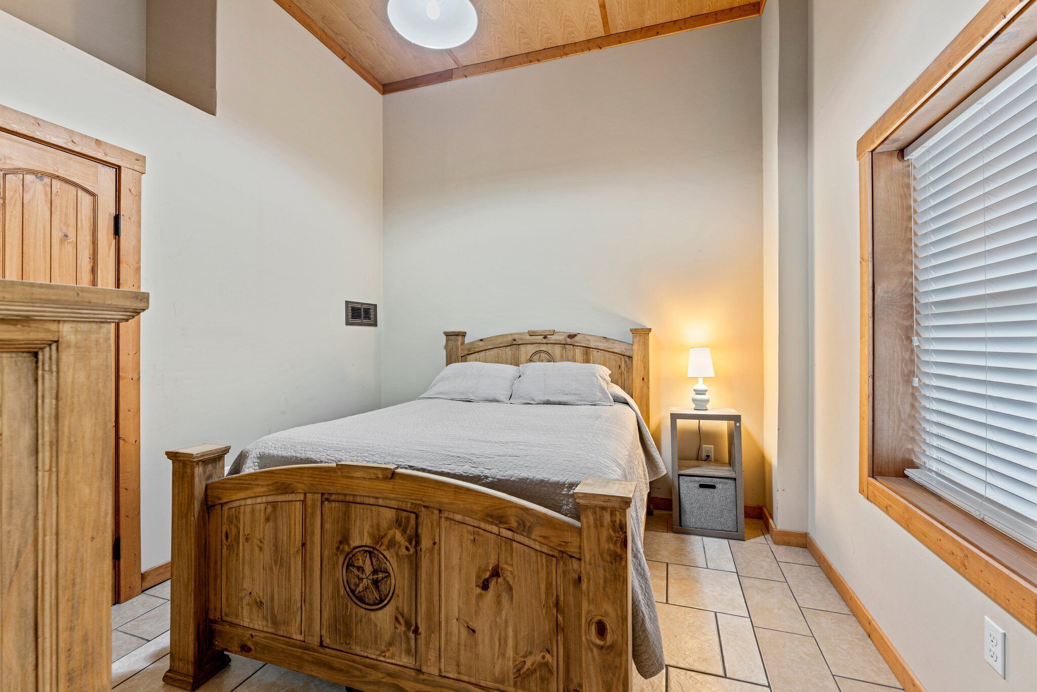 A wooden bed in a room with a window and a nightstand.