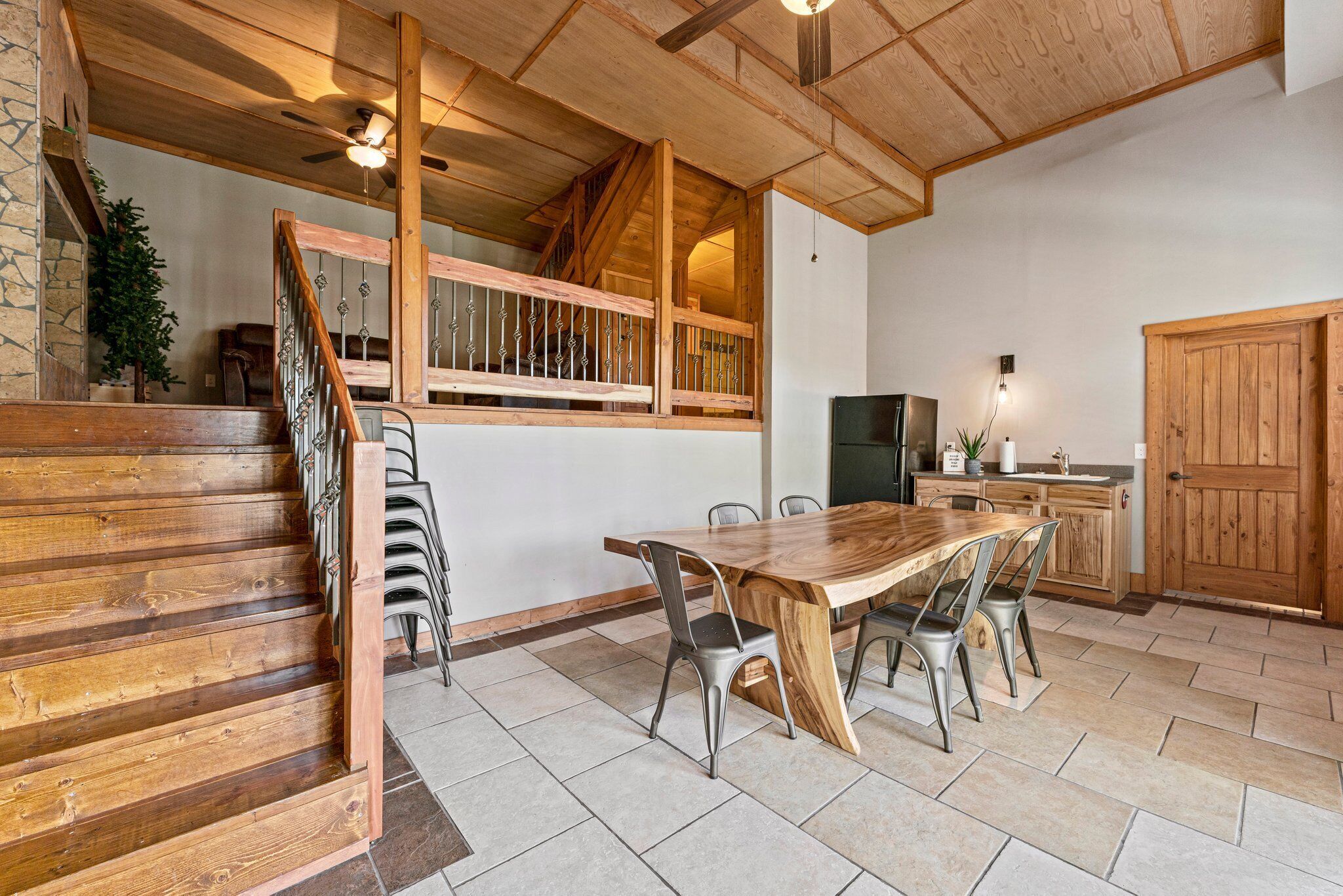 Een houten trap leidt naar een hoger gelegen eetgedeelte met een grote tafel en stoelen.