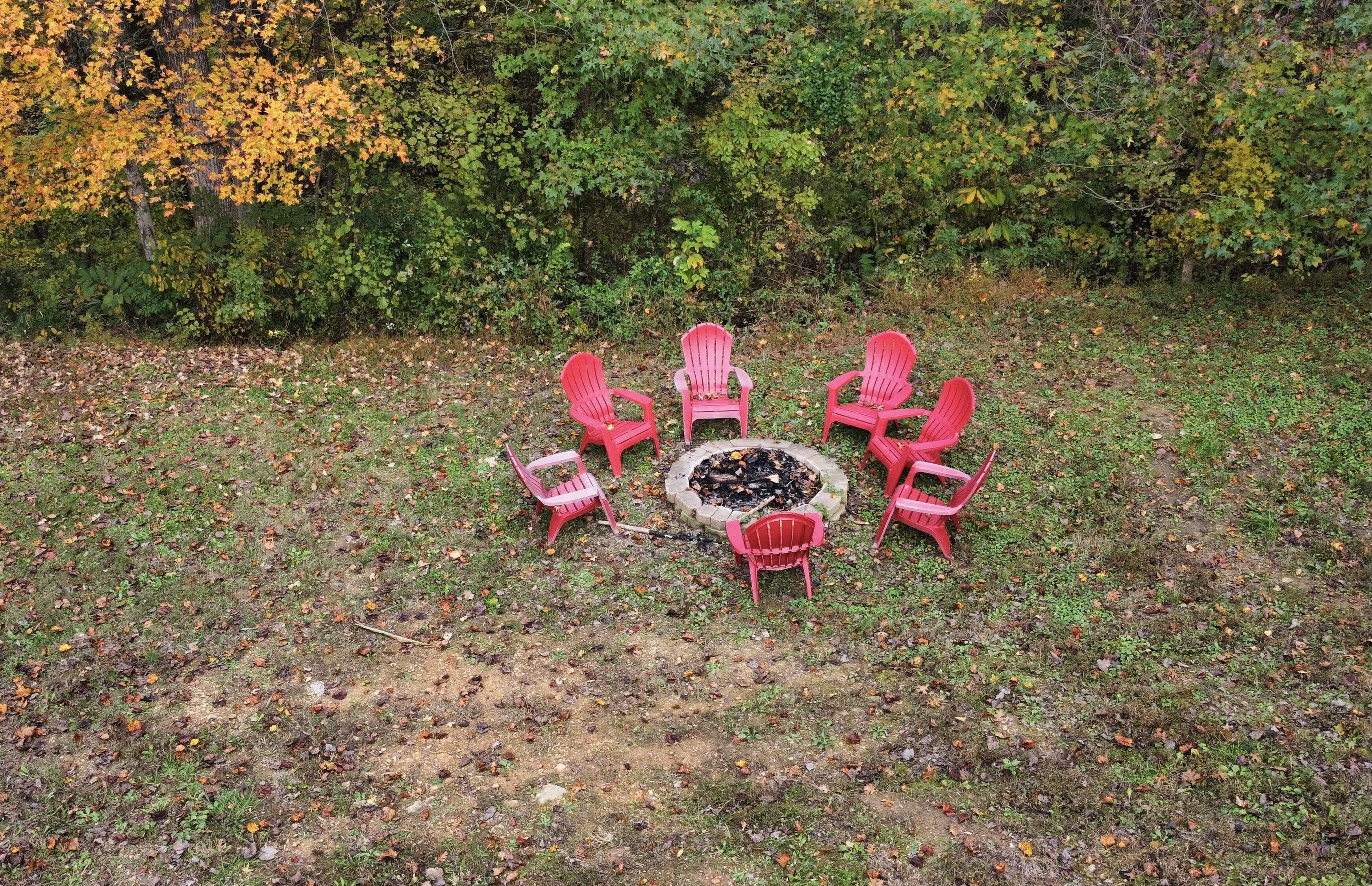Seis sillas Adirondack rojas dispuestas en círculo alrededor de un brasero en un entorno exterior.