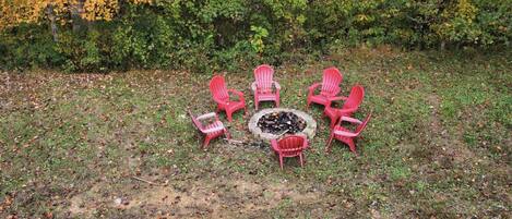 Seis sillas Adirondack rojas dispuestas en círculo alrededor de un brasero en un entorno exterior.