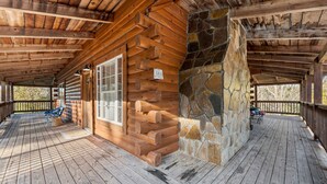 A log cabin with a stone fireplace, wooden deck, and a covered porch area.
